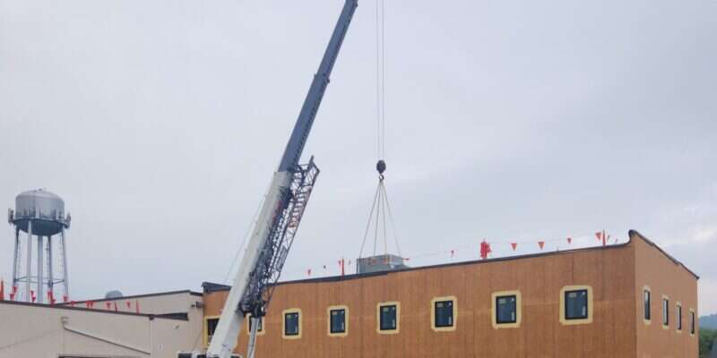 Crane hoisting a packaged rooftop HVAC unit onto the roof of the Shickel Corporation office addition in Bridgewater, Virginia
