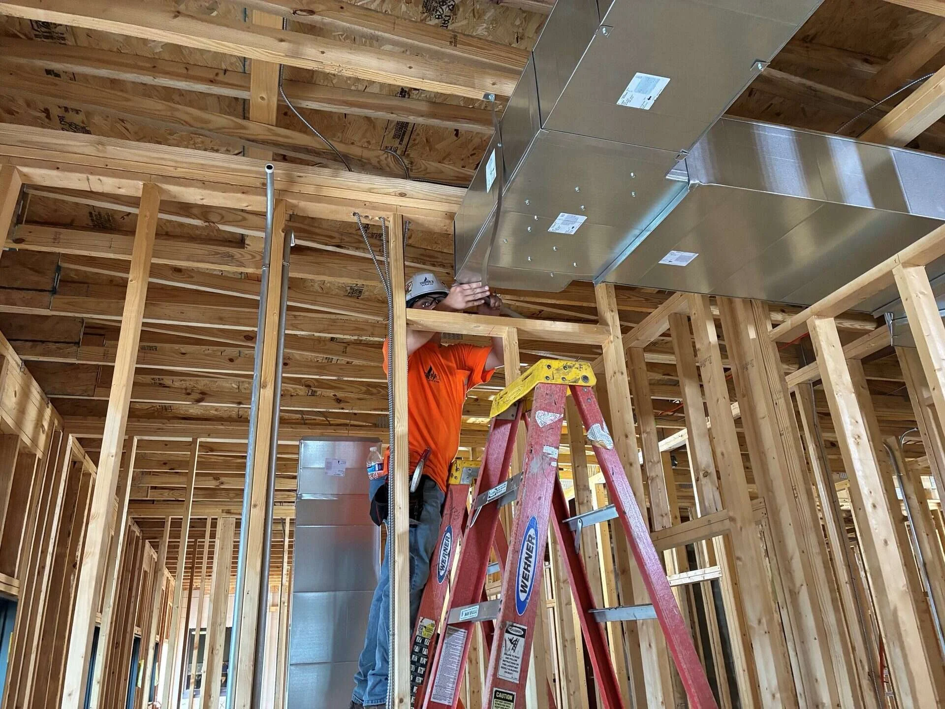 Young's Mechanical Solutions technician securing a rectangular sheet metal trunk duct to overhead framing