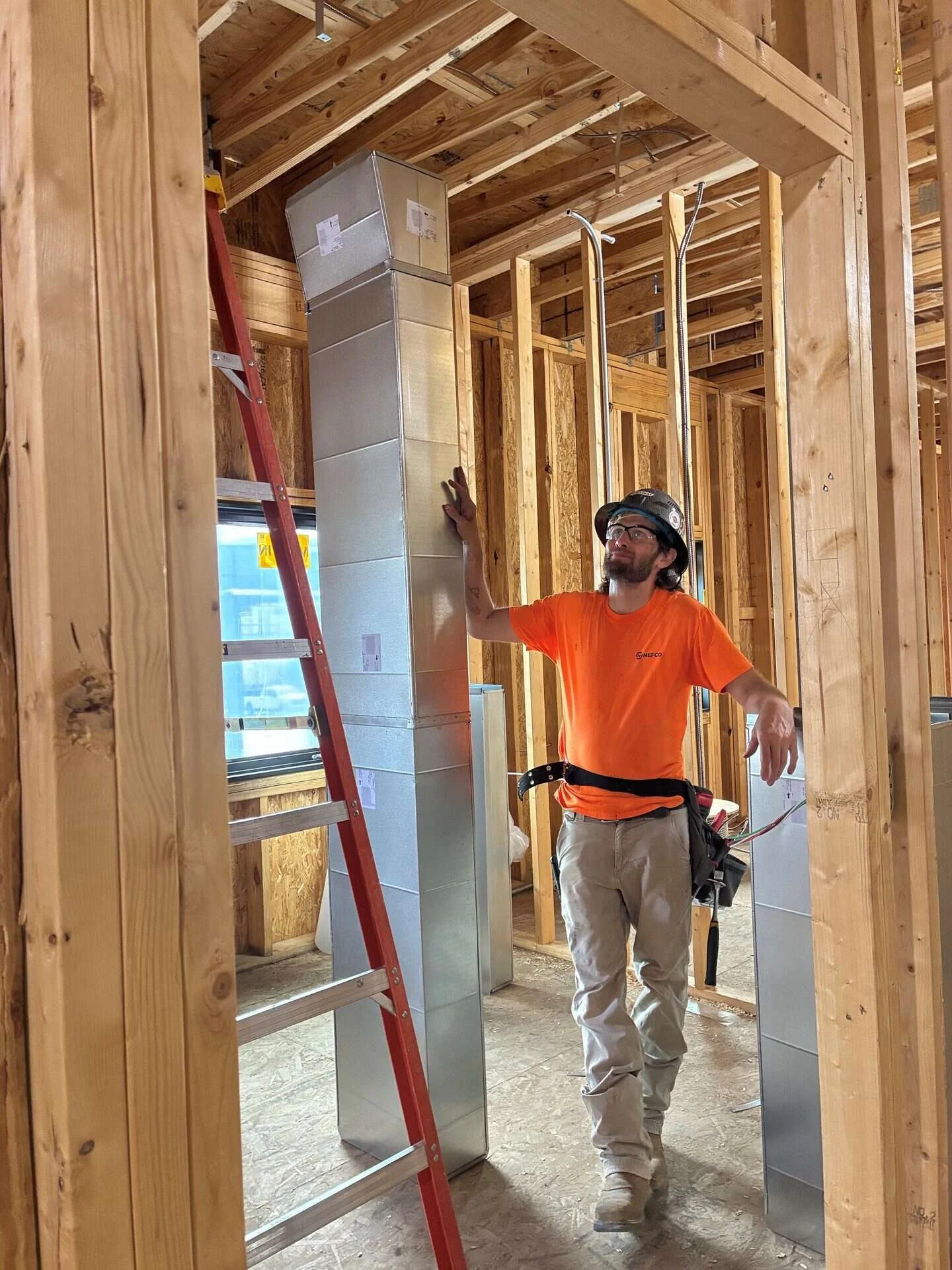 Sheet metal technician beside a full-height vertical duct riser in a framed mechanical chase