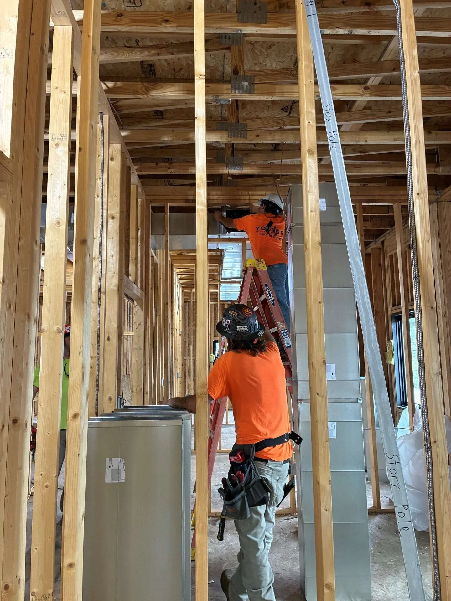 Two Young's Mechanical Solutions technicians installing duct risers and overhead ductwork in a framed commercial building