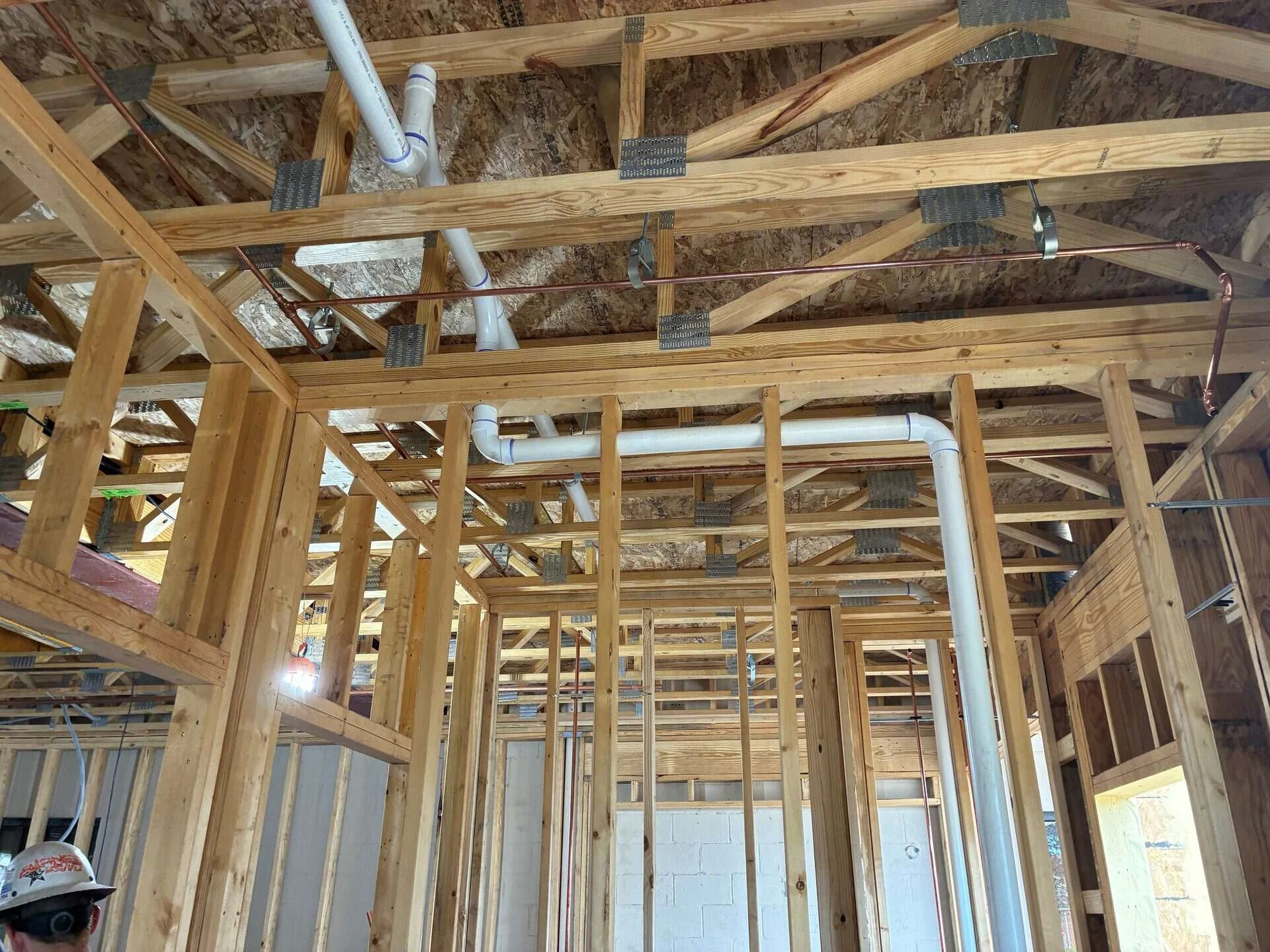 Copper water lines and PVC drain, waste and vent piping run through roof trusses during plumbing rough-in on a commercial building in Bridgewater, Virginia