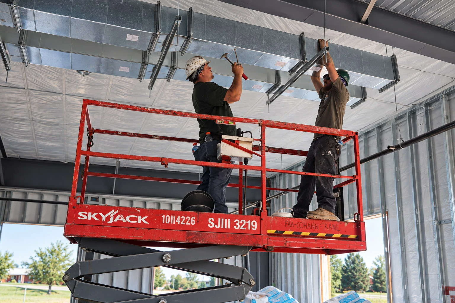 Young's Mechanical Solutions sheet metal crew installing commercial ductwork from a scissor lift at the New Beginnings Church project