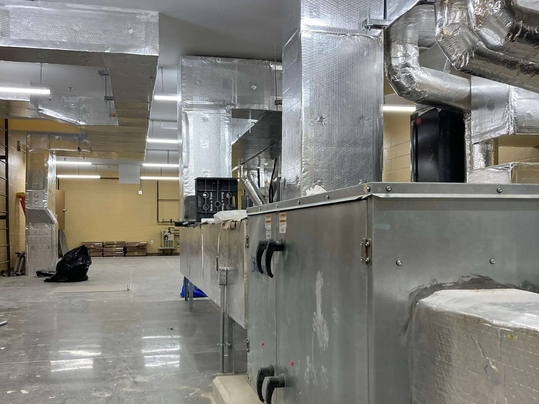 Row of commercial air handling units and insulated ductwork in a mechanical room installed by Young's Mechanical Solutions